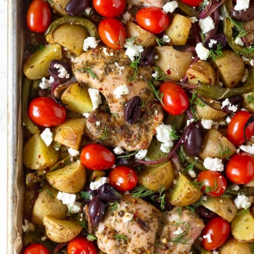 Greek sheet pan chicken with roasted potatoes, peppers, and onions, cherry tomatoes, Kalamata olives, and feta. It is garnished with fresh dill.