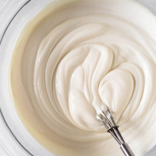 Greek yogurt frosting in a glass bowl with a small metal whisk in it.