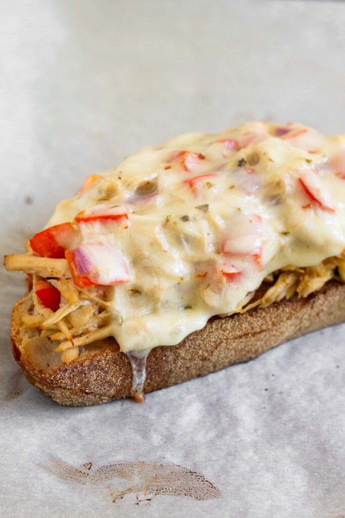 A close up of toasted bread topped with chicken salad and melted cheese on top.
