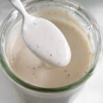 Healthy coleslaw dressing in a jar with a spoon full of dressing overtop of it. In front of the jar is half a juiced lime.