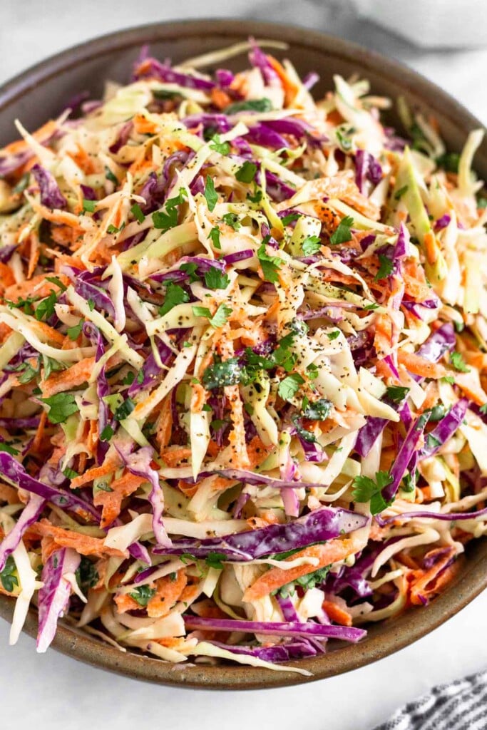 A large bowl of healthy coleslaw garnished with fresh cilantro and black pepper.