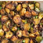 Large white bowl filled with crispy air fryer brussel sprouts garnished with sesame seeds and green onions.