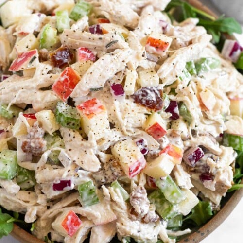 Chicken salad with apples, walnuts, celery, and dates overtop fresh arugula in a bowl.