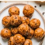 Peanut butter oatmeal protein balls stacked on top of each other on a plate. Some oats and chocolate chips are on scattered around the plate.
