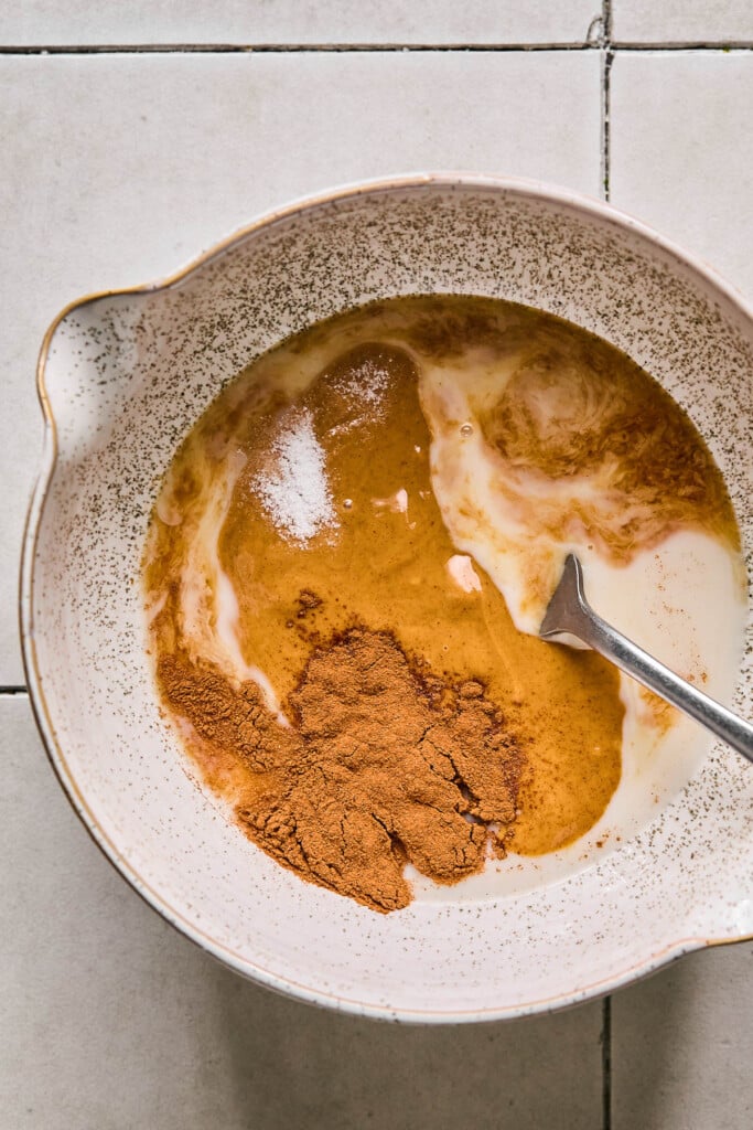 Peanut butter, milk, honey, cinnamon, and salt in a mixing bowl before it is mixed together. There is also a fork in the bowl.