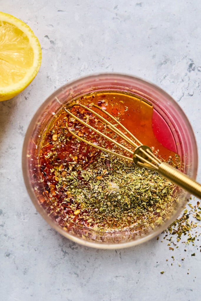 Glass jar filled with red wine vinegar, olive oil, lemon, and spices. Next to it is half a lemon.