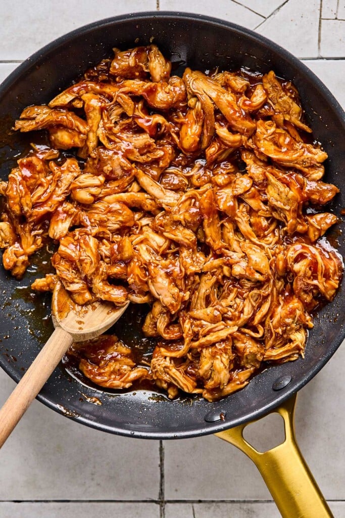 Shredded bbq chicken in a skillet with a wooden spoon in it.