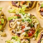 Chicken tostadas with refried beans, seasoned shredded chicken, lettuce, pico de gallo, queso fresco, and cilantro on them.
