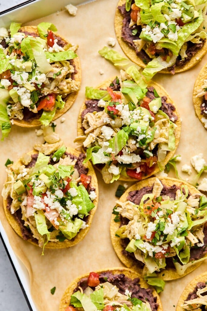 A baking sheet with chicken tostadas with beans, shredded chicken, lettuce, pico de gallo, cheese, and cilantro.