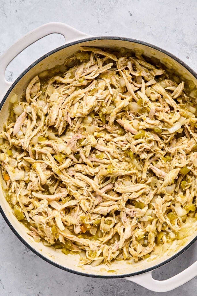 Large enameled pan with a mixture of shredded chicken, saut&eacute;ed onions, and green salsa.