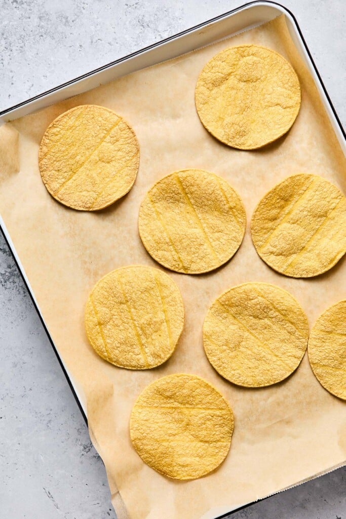 Overhead shot of a baking sheet lined with parchment paper with crispy corn tortilla shells on it.