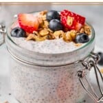 A jar of protein chia pudding topped with strawberries, blueberries, and granola. The jar is sitting on a plate.