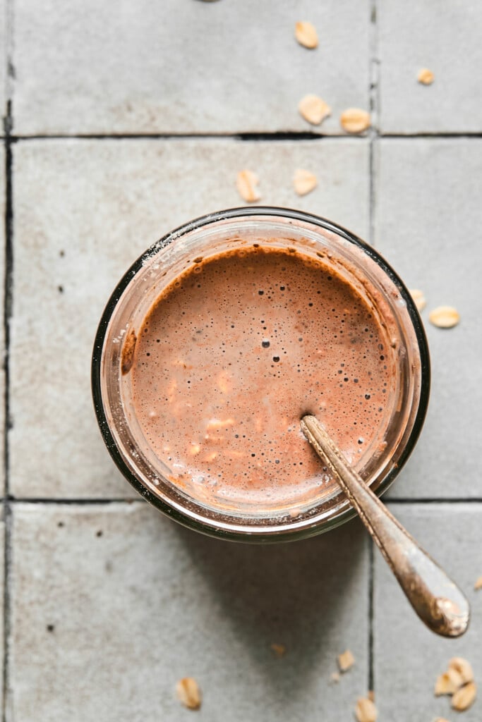 Overhead shot of a jar filled with a liquid mixture of milk, cinnamon, cocoa powder, and rolled oats with chia seeds in it.