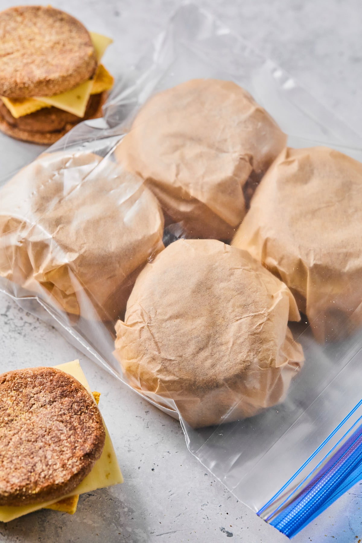 Postpartum freezer breakfast sandwiches wrapped in parchment paper in a large plastic bag. Next to the bag are two sandwiches that haven't been wrapped up yet.