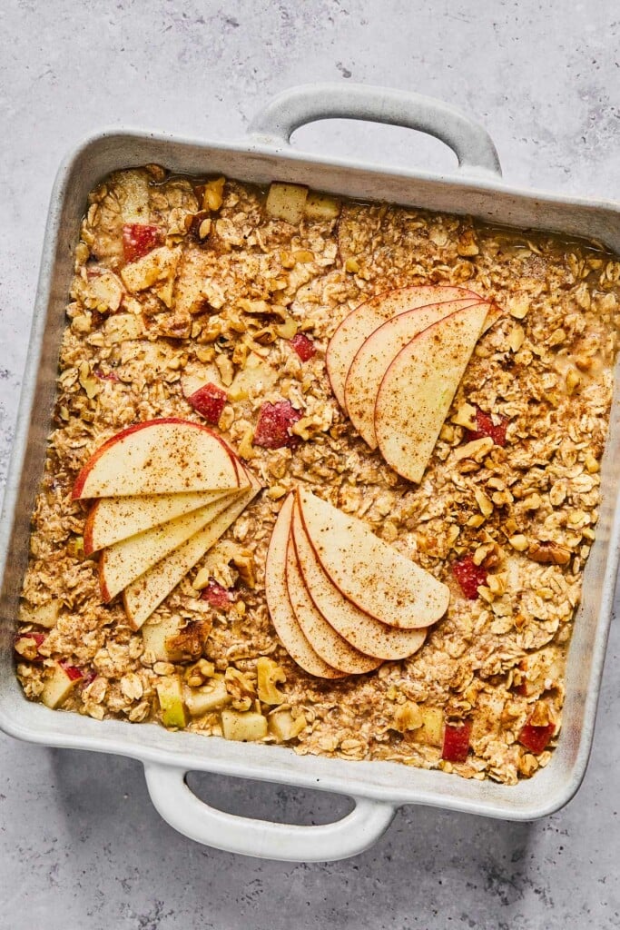 A large baking dish filled with an oatmeal mixture with apples and walnuts before it is baked. The mixture is topped with some sliced apples.