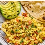 A plate of migas, sliced avocado, and tortillas. The migas are garnished with salsa and cilantro.