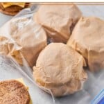 Postpartum freezer breakfast sandwiches wrapped in parchment paper in a large plastic bag. Next to the bag are two sandwiches that haven't been wrapped up yet.