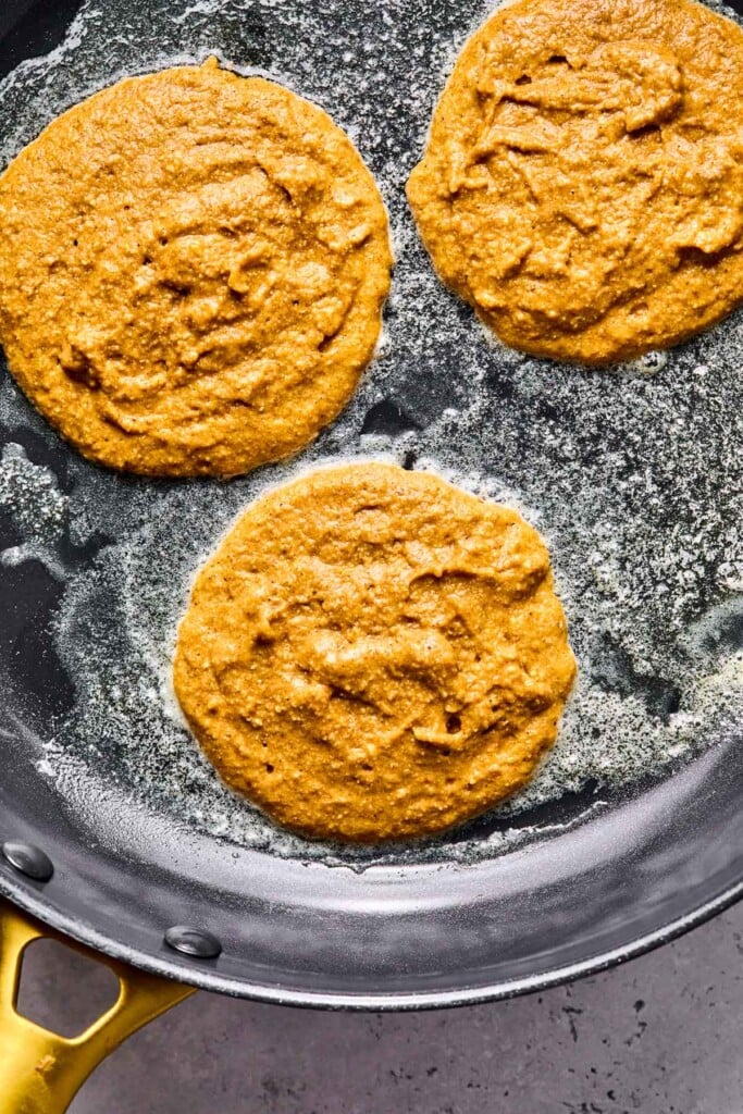 Large skillet with pumpkin pancakes on it before they are flipped.