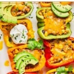 An overhead shot of taco stuffed peppers with melted cheese topped with sour cream, avocado slices, and cilantro in a white casserole dish.