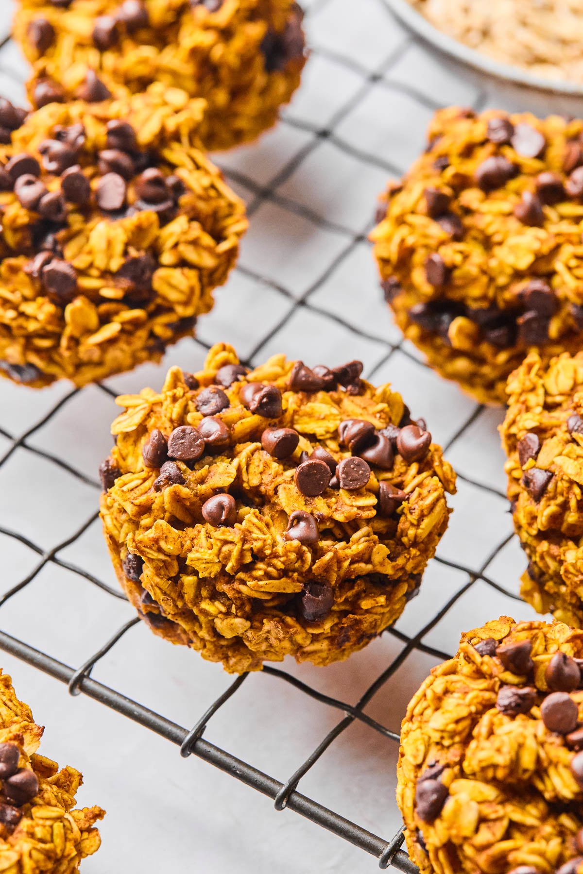 Pumpkin oatmeal muffins on a metal cooling rack. In the back off to the side is a bowl of rolled oats.