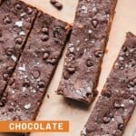 Chocolate protein bars spread out on a piece of parchment paper with mini chocolate chips around them.