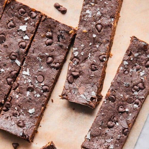 Chocolate protein bars spread out on a piece of parchment paper with mini chocolate chips around them.