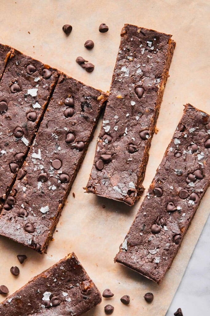 Chocolate protein bars spread out on a piece of parchment paper with mini chocolate chips around them.
