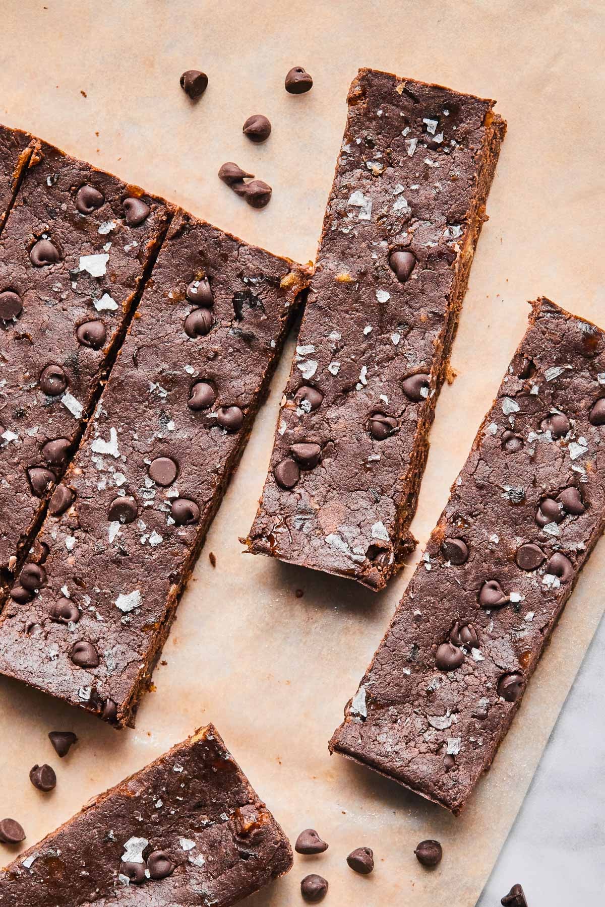 Chocolate protein bars spread out on a piece of parchment paper with mini chocolate chips around them.