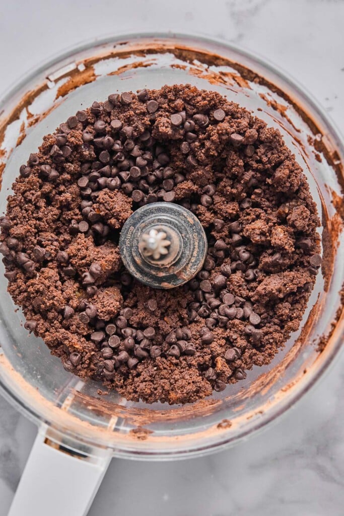 Overhead shot of slightly crumbly but wet chocolate batter with mini chocolate chips in a food processor.