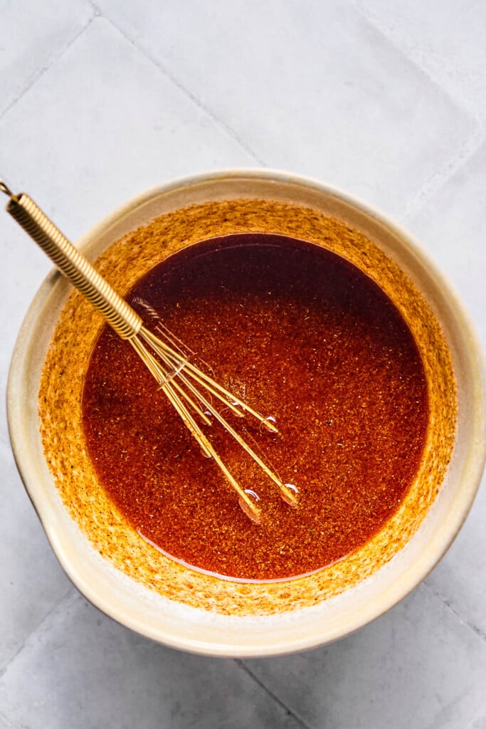 Hot honey chicken marinade in a white bowl with a whisk in it.