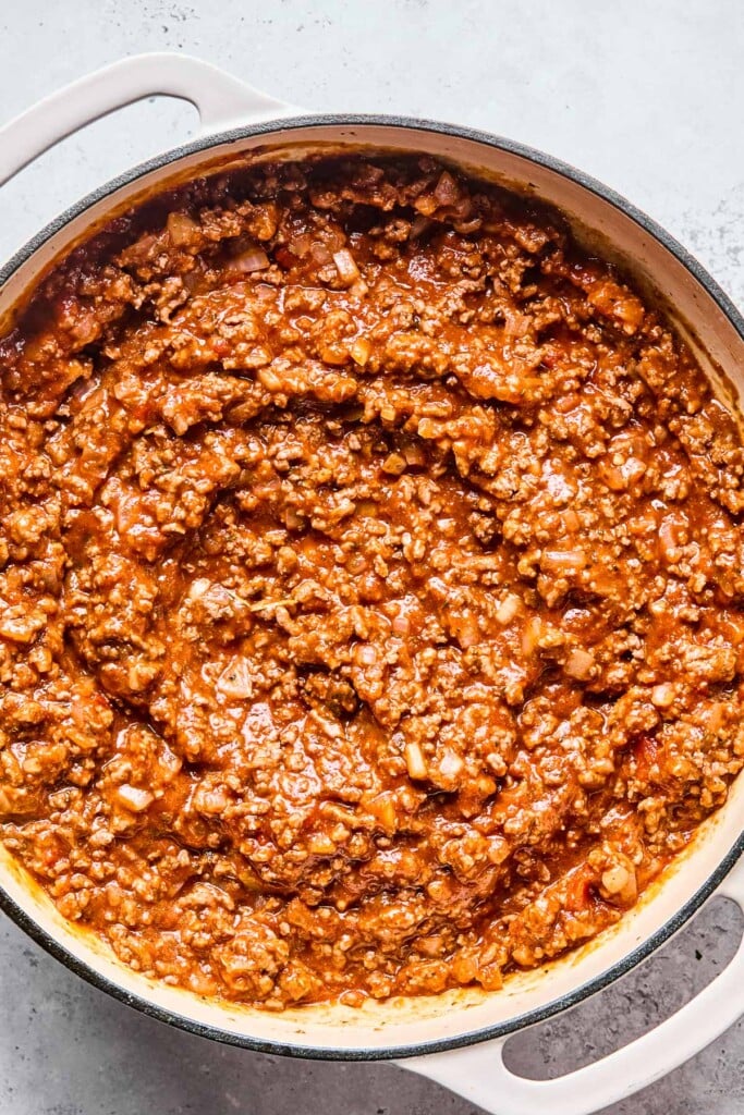Overhead shot of a enameled pan filled with ground beef and onions mixed with pasta sauce.