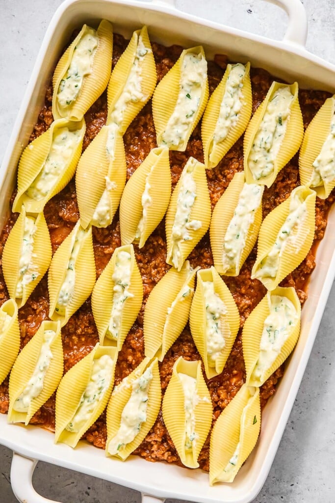 A large baking dish with meat sauce spread across the bottom with pasta stuffed shells on top of it.