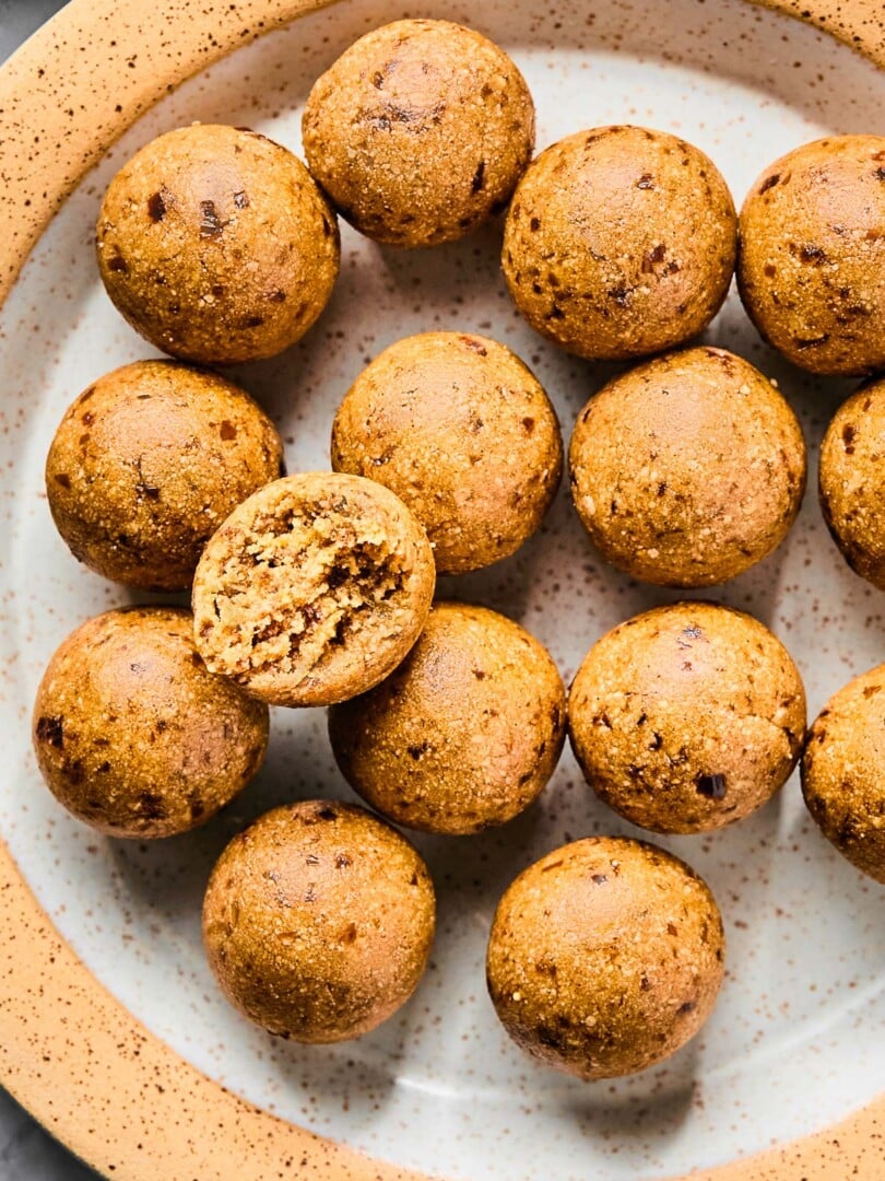 A plate of peanut butter protein balls. One of the balls is on top of the rest and it has a bite taken out of it.
