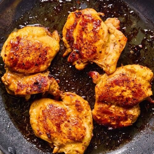 Skillet with seasoned pan fried chicken thighs in it.