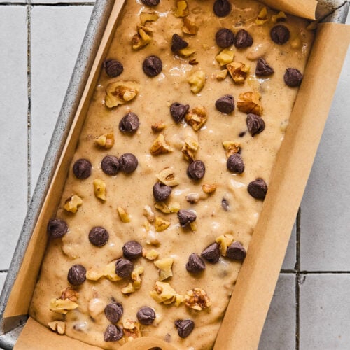 Chocolate chip banana bread batter with walnuts in a loaf pan lined with parchment paper.
