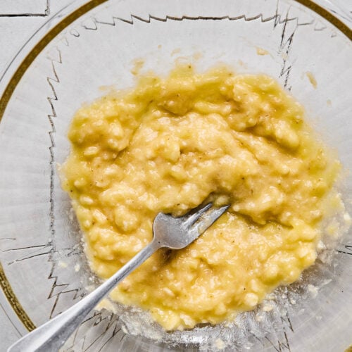 Glass mixing bowl with mashed bananas and a fork in it.