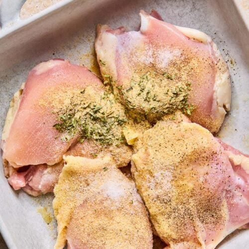 Raw chicken thighs sprinkled with spices in a baking dish.