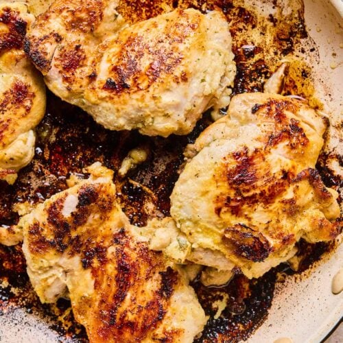 Seasoned cooked chicken thighs in a skillet.