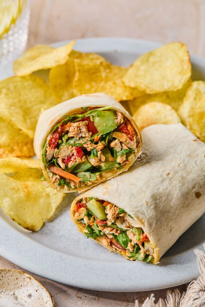 Chicken salad wrap with veggies on a plate with some potato chips.