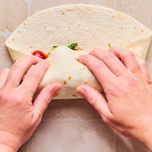 A large tortilla stuffed with chicken and veggies that is being wrapped up.