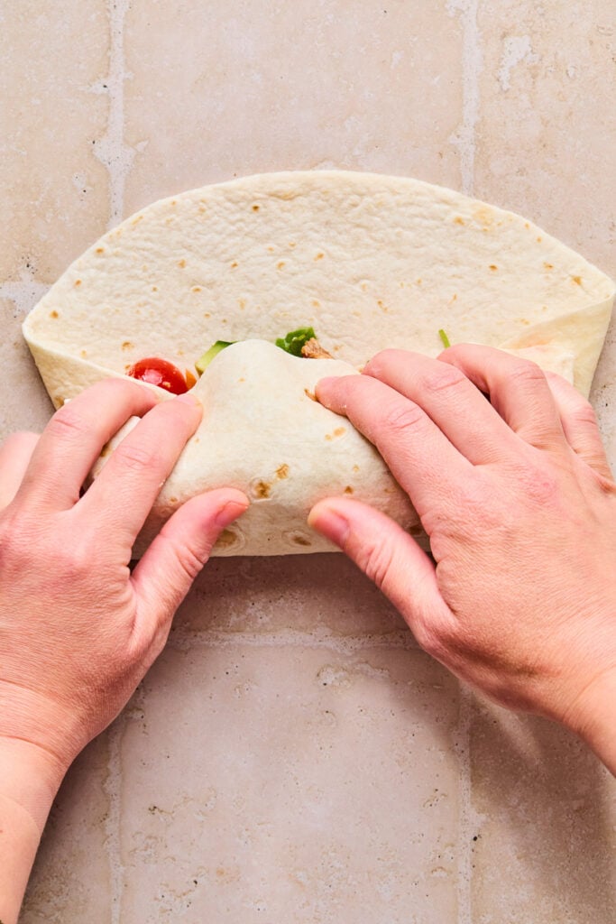 A large tortilla stuffed with chicken and veggies that is being wrapped up.