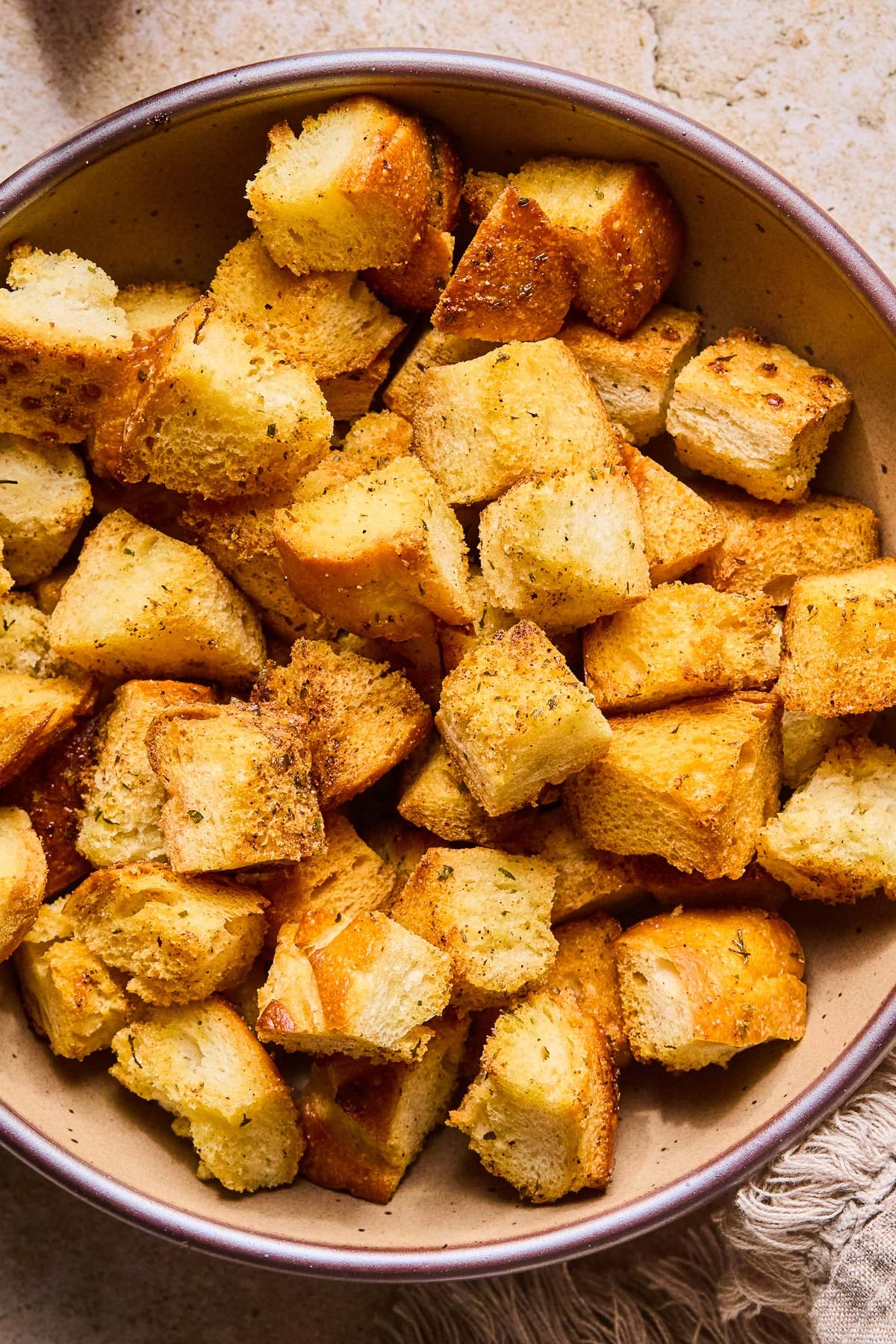A close up of a bowl of sourdough croutons. Next to the bowl is a tan linen towel.