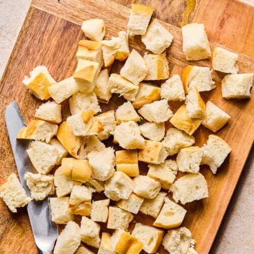 A cutting board with cubed bread and a knife on it.