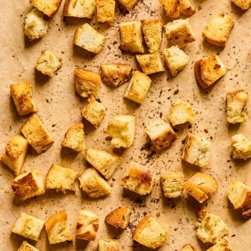Croutons from sourdough bread spread out on a piece of parchment paper.