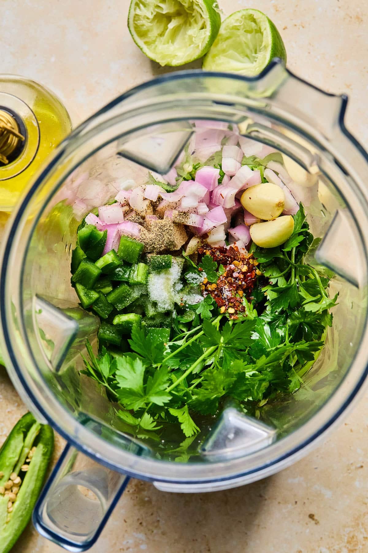 Blender will olive oil, fresh parsley, fresh cilantro, chopped jalape&ntilde;o, chopped shallot, two garlic cloves, and spices before it is blended.