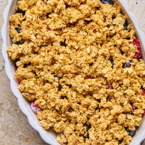 A small oval casserole dish of filled with mixed berries topped with a sticky oatmeal crumble before it is baked.