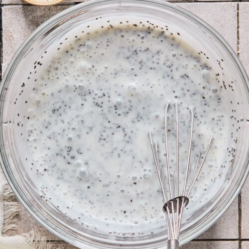 Overhead shot of a large bowl with a mixture of kefir and chia seeds before it gels. A spoon is also in the bowl. Around the bowl is a bowl of chia seeds and a white kitchen towel.