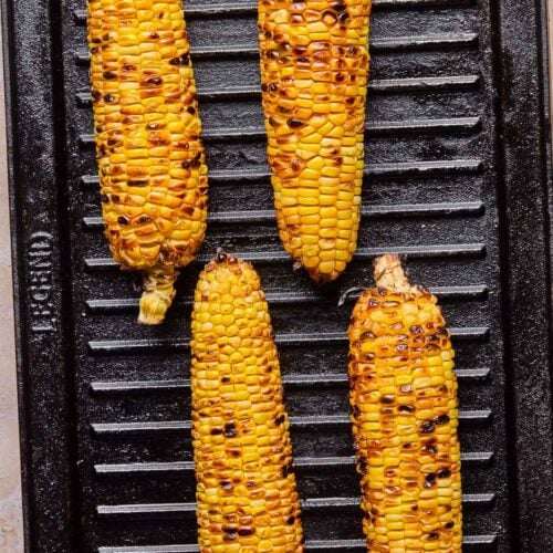 Four ears of corn on the cob cooking on a grill pan. They all have char marks on them.