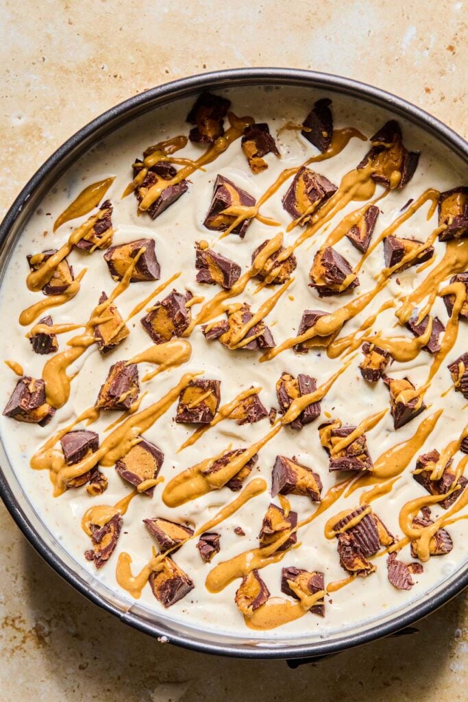 Overhead shot of a Reese cup ice cream cake in a cake pan. It is topped with chopped Reese's cups and drizzled with peanut butter.