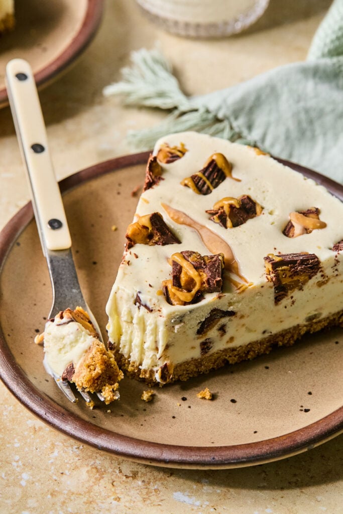 A plate with a slice of Reese’s peanut butter cup ice cream cake. A fork is on the plate with some of the ice cream cake on it. Behind the plate is a green kitchen towel, a glass of milk, and another plate.